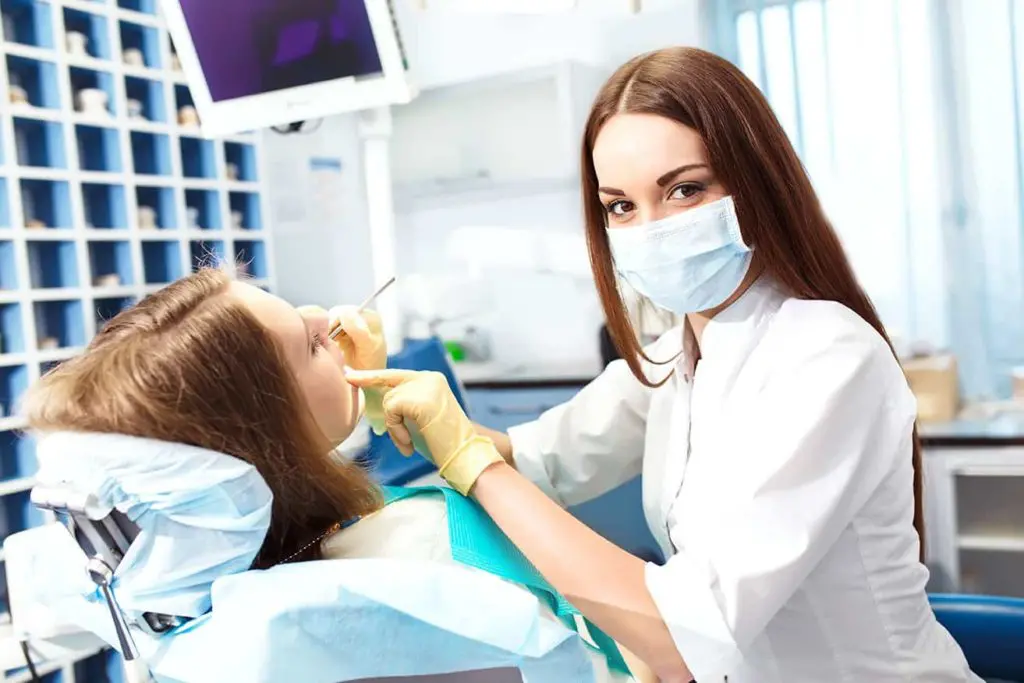Klinikai fogászati higiénikus képzés visszanézhető órákkal és online jegyzetekkel a Pannon Kincstár iskolában. Barna hajú fogorvos kezeli a páciensét.