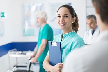Az általános ápoló hölgy kék nővérruhában áll betegei és az orvosok között.