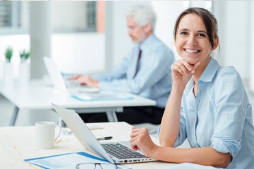 Vállalkozási mérlegképes könyvelő hölgy kék ingben dolgozik számítógépén.