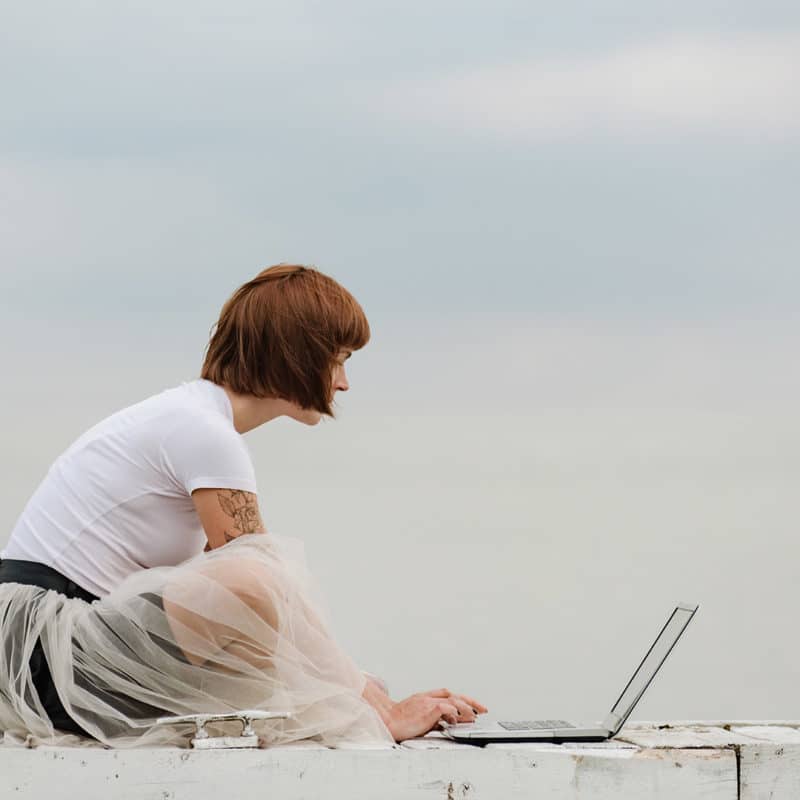 Vörös, rövid hajú lány egy laptopot figyel fehér háttér előtt. Pannon Kincstár