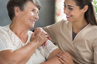 Egy szociális és mentálhigéniés szakgondozó hölgy mosolyogva beszélget egy idős páciensével.