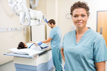 Kék nővérruhás radiográfiai asszisztens segíti a szakorvost, aki egy pácienst gyógyít.