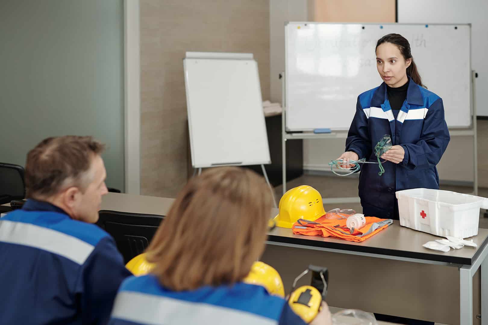 Női munkavédelmi oktató különböző biztonsági felszereléseket mutat be munkásoknak. Munkavédelmi előadó képzés a Pannon Kincstárban!