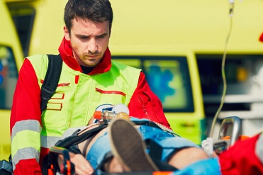 Barna hajú mentőápoló férfi cipeli a mentőautó felé megmentett betegét.