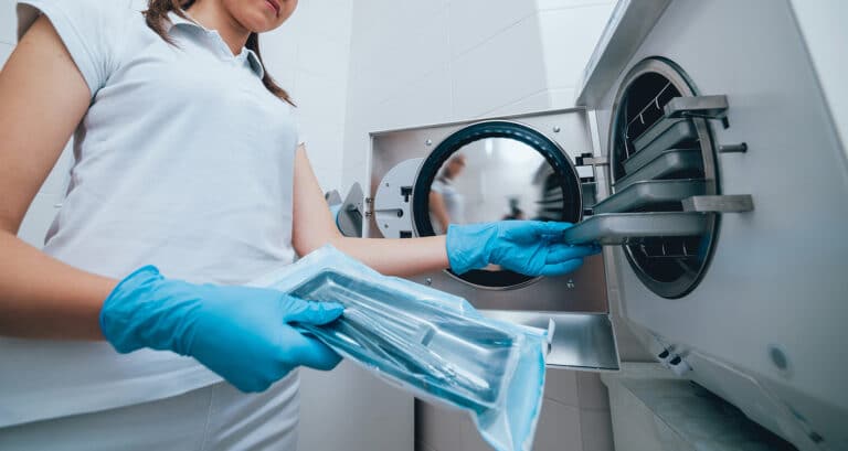 Fertőtlenítő-sterilező nő orvosi eszközöket sterilizál, sterilizáló eszköz segítségével. Fertőtlenítő-sterilező képzés a Pannon Kincstárban, szakmai cikk