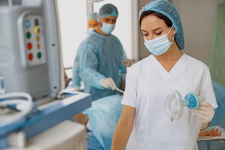Aneszteziológiai szakasszisztens nő a műtőben áll orvosi ruhában és altató orvosi eszközt tartva a kezében segédkezik. Aneszteziológiai szakasszisztens képzés a Pannon Kincstárban, szakmai cikk
