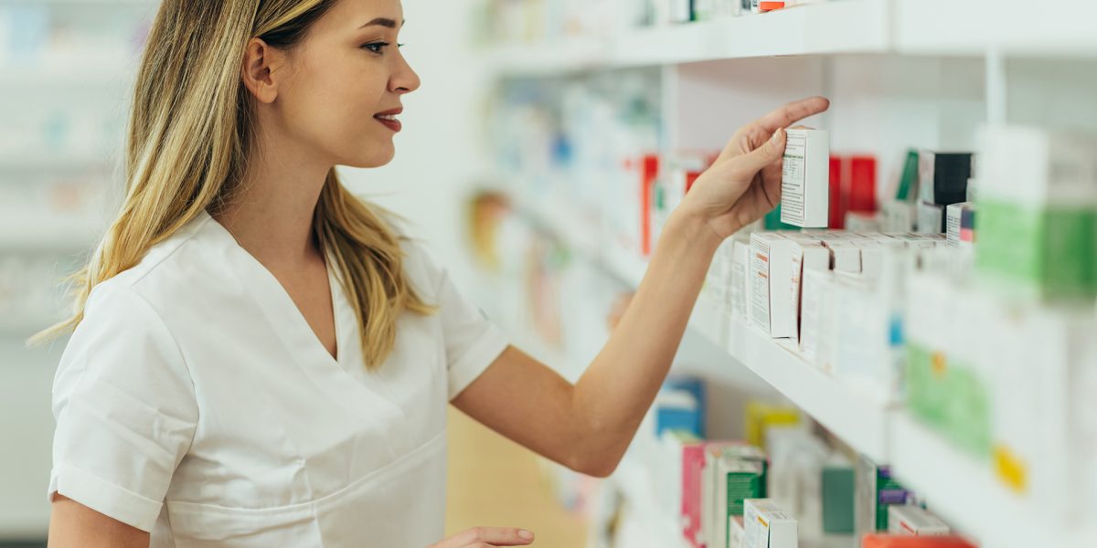 Portrait of a beautiful female pharmacist working in a pharmacy and checking medications on a shelf