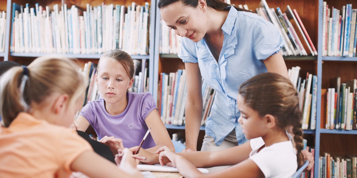 Overseeing her students work. A pretty young teacher helping her students with their work in the library
