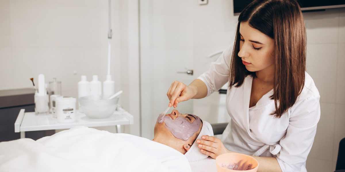 Cosmetologist applying mask on woman's face in beauty salon.