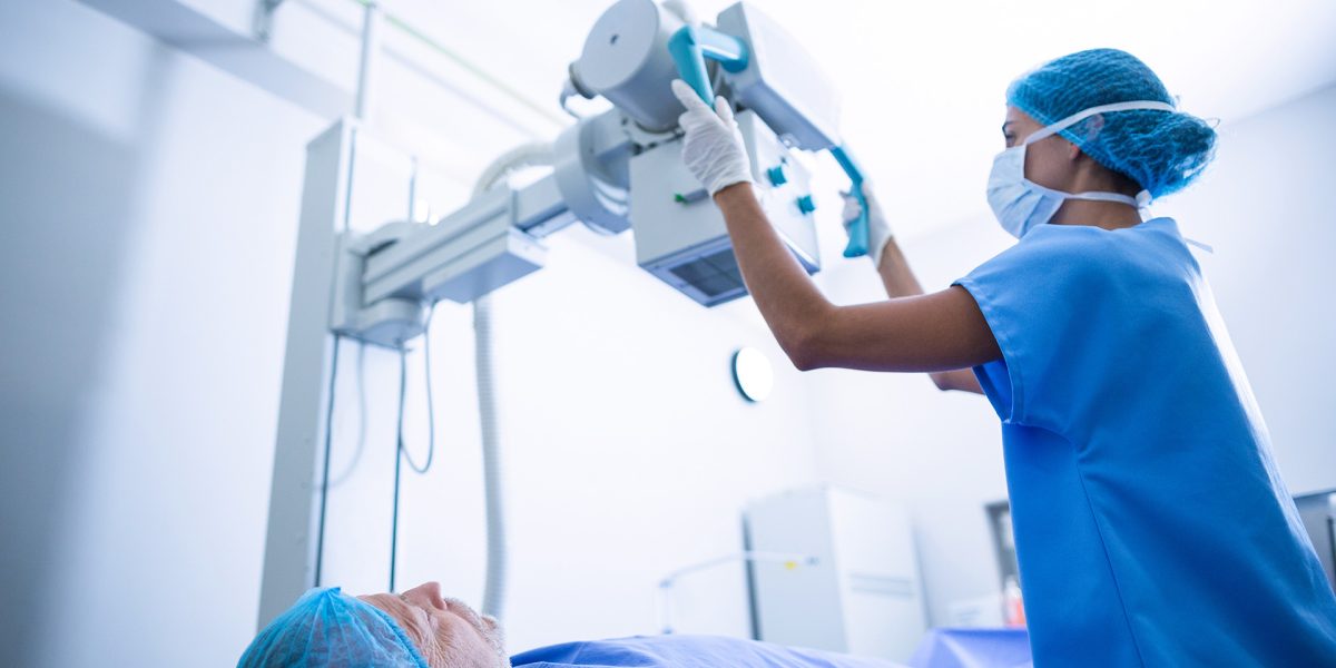 Nurse adjusting x-ray machine over patient in hospital