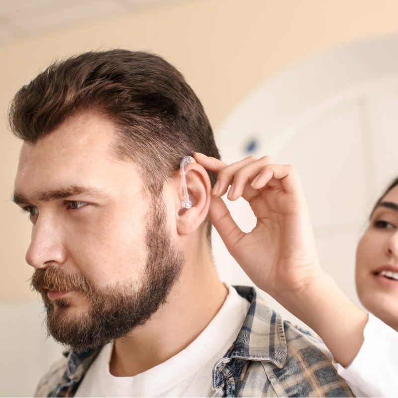 Audiológiai asszisztens és hallásakusztikus képzés a Pannon Kincstárnál. 100% ONLINE elmélettel Mosolygós audiológiai asszisztens egy fiatal férfi hallásjavító készülékét igazítja