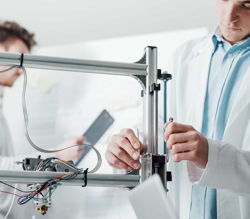 Digitális fogtechnikus képzés, Pannon Kincstár Fogtechnikus férfi 3D nyomtatót használ orvosi köpenyben. Digitális fogtechnikus képzés a Pannon Kincstár!