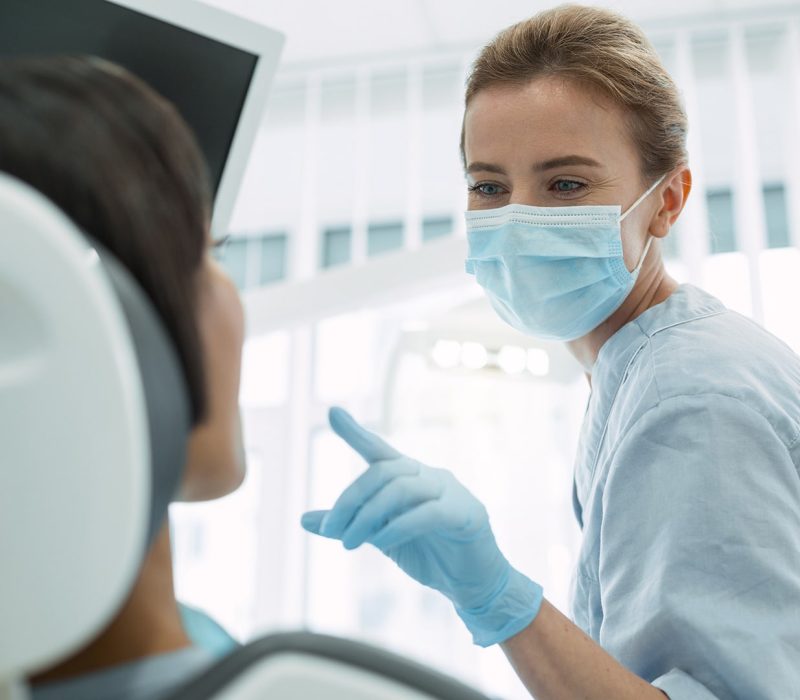 Klinikai fogászati higiénikus képzés Egy klinikai fogászati higiénikus nő orvosi kesztyűben és maszkban figyeli egy páciens fogait.