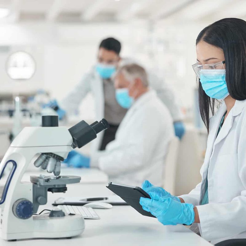 Klinikai laboratóriumi asszisztens nő dolgozik egy modern laborban, védőszemüveget és laboratóriumi köpenyt visel. Klinikai laboratóriumi asszisztens képzés a Pannon Kincstárban!