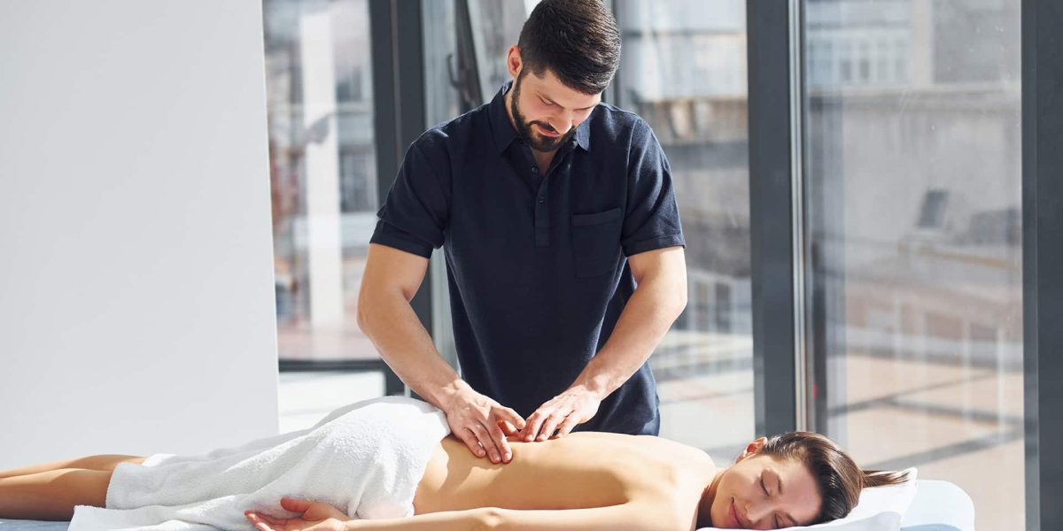 Gyógymasszőr férfi egy nőt masszíroz letisztult környezetben. Gyógymasszőr képzés, Pannon Kincstár